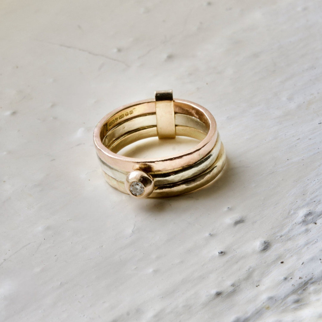A three-band 9ct gold ring with a central white diamond, set in a molten 9ct gold ball, on a textured white background.