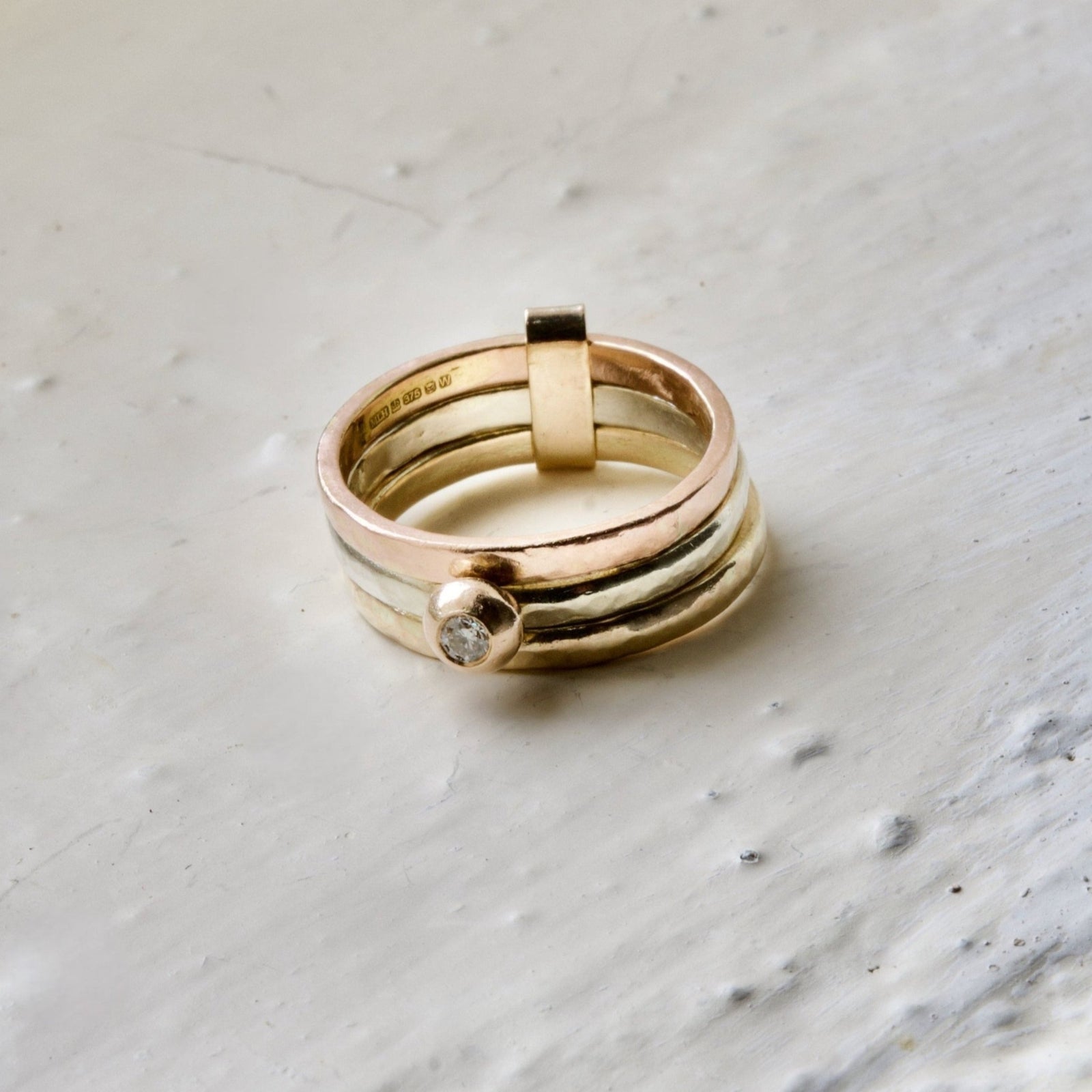 A three-band 9ct gold ring with a central white diamond, set in a molten 9ct gold ball, on a textured white background.