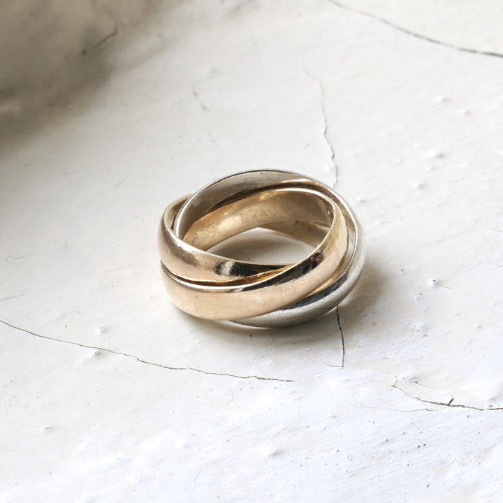 A sterling silver and yellow gold triple interlocking  sentimental piece of jewellery otherwise know as aring. Placed on rustic white cotswold stone.