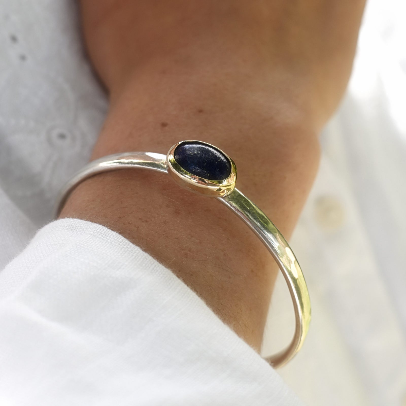 Gold bracelet with a dark stone on a wrist against a neutral background