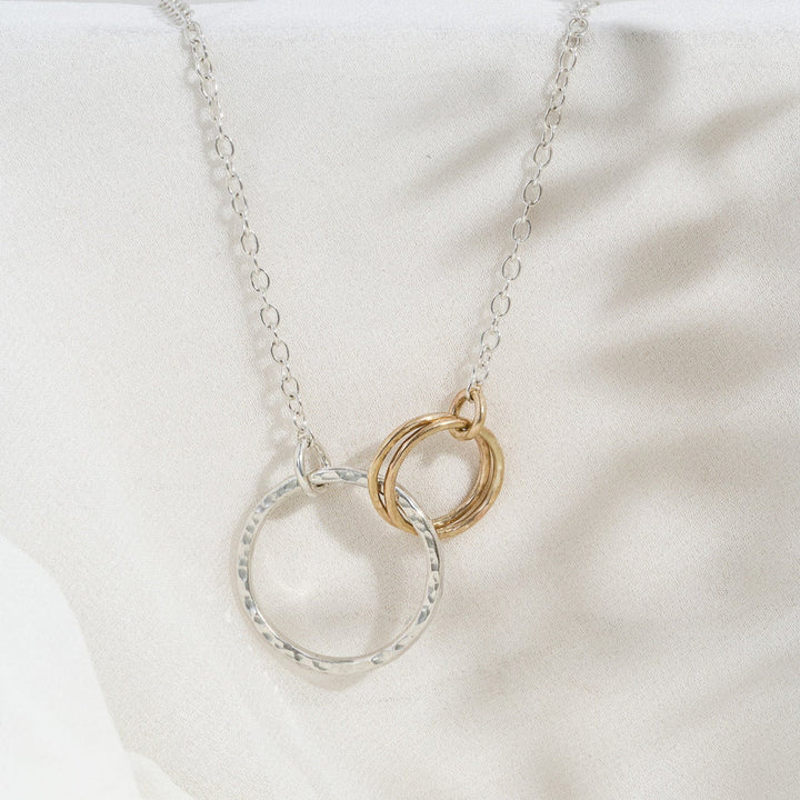 A silver necklace featuring two gold circles and a gold chain, displayed on a white fabric surface.