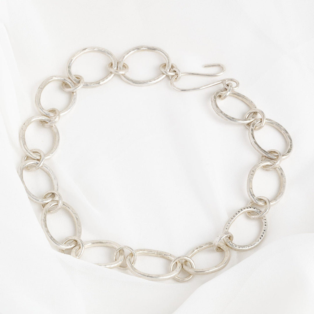 A sterling silver chain necklace with a series of linked rings, featuring adjoining circular links with a diamond sparkle in the center, displayed against a white background.
