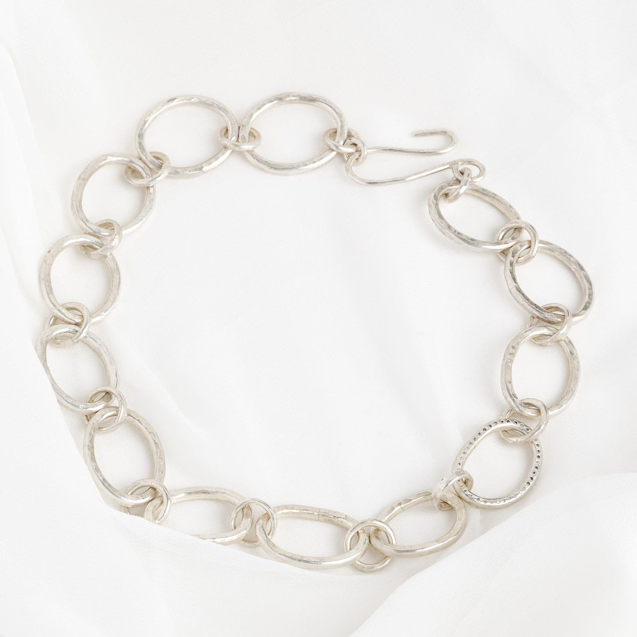 A sterling silver chain necklace with a series of linked rings, featuring adjoining circular links with a diamond sparkle in the center, displayed against a white background.