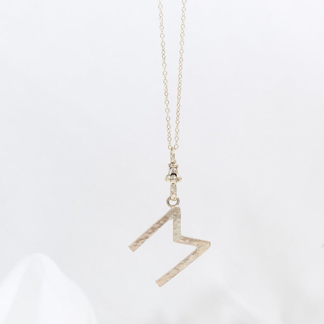 A gold letter pendant necklace on a white background, with the pendant in the shape of the letter &