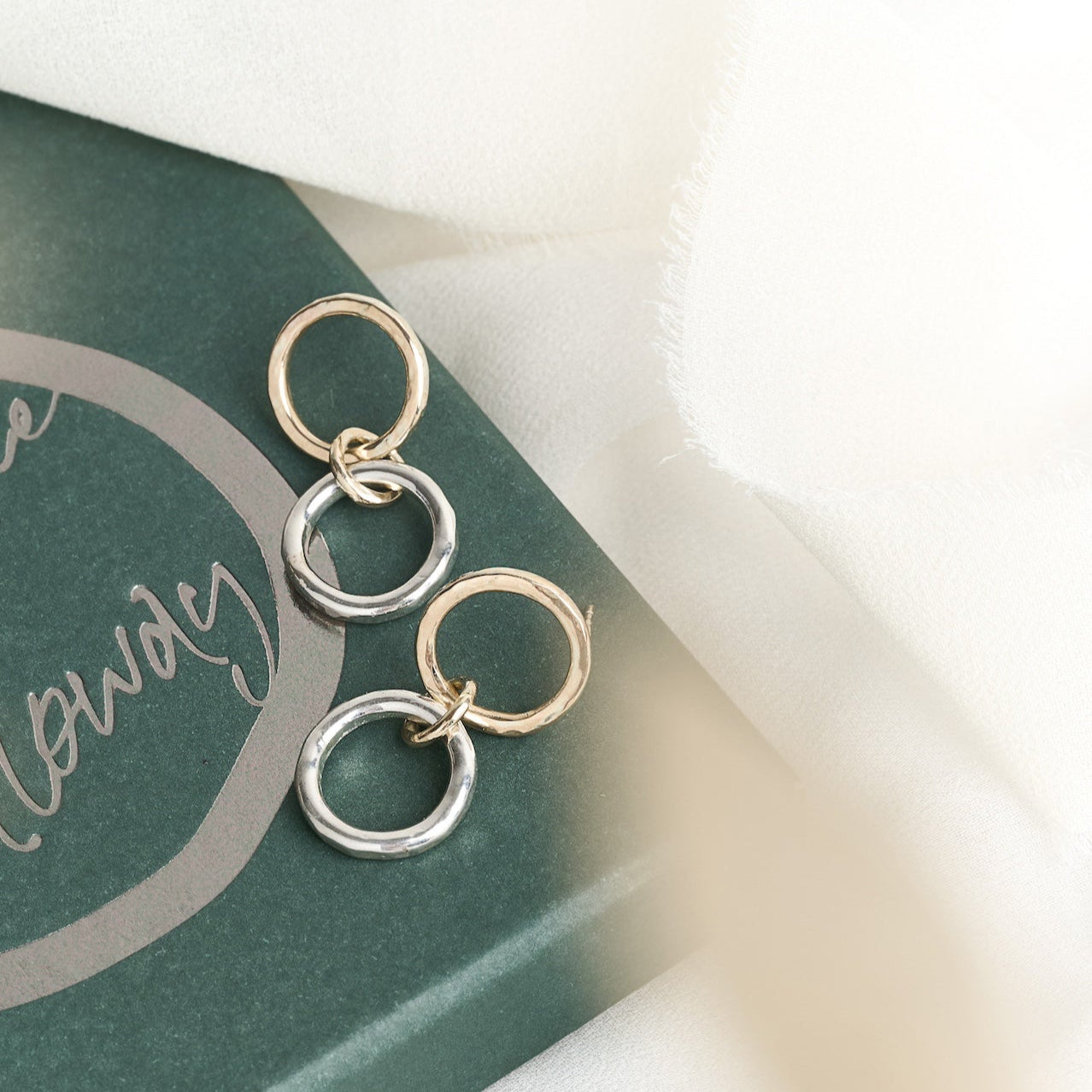 Pair of gold and silver hoop earrings on a green card with text.