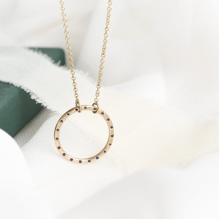 A 9ct gold pendant with a chunky design featuring deep blue sapphires, displayed on a white fabric surface.