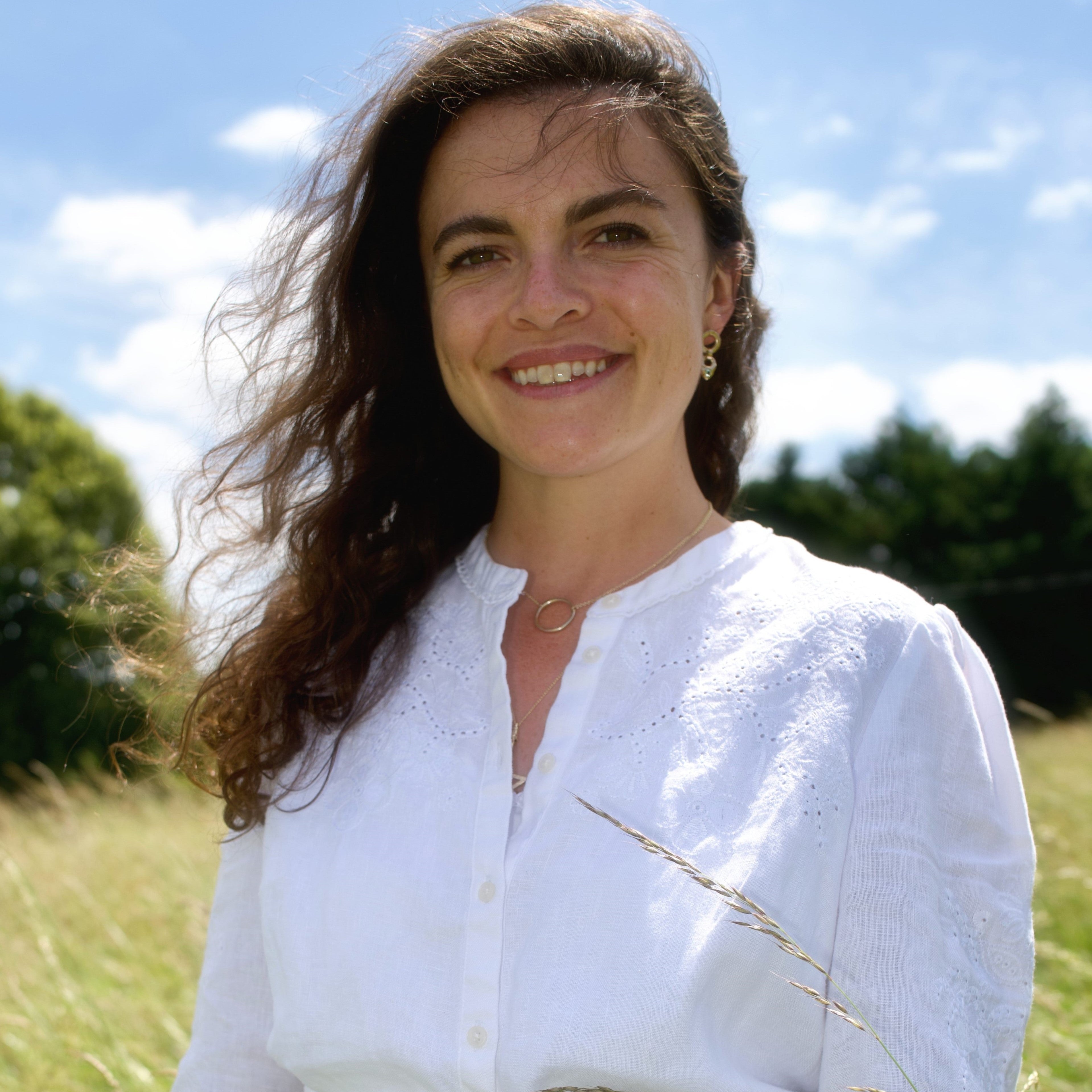 Woman in a white dress with a gold belt standing in a grassy field.