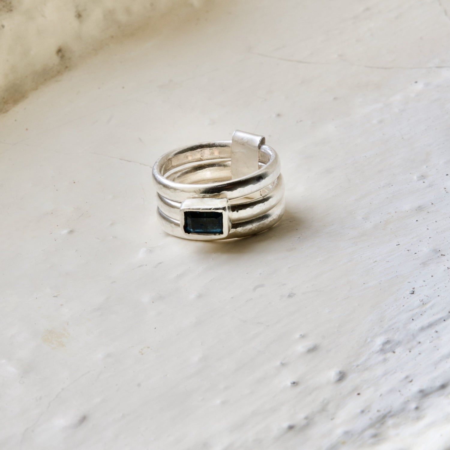A sterling silver and blue topaz stack ring placed on a textured surface.